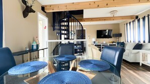 A modern living room with a glass dining table, leather chairs, a staircase, and a TV. - Waterfront home on Perch Lake outside Traverse City. Hot tub. Pool table. (South Boardman)