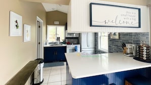 A modern kitchen with a central island, a dining area with blue chairs, and a welcoming sign. - Waterfront home on Perch Lake outside Traverse City. Hot tub. Pool table. (South Boardman)