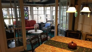 Une pièce chaleureuse avec une table à manger, des chaises, un canapé rouge, des fauteuils en osier et un piano.