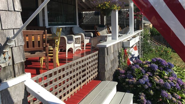 Un espace extérieur abrité, aménagé avec des meubles en osier, un drapeau rouge et blanc à rayures et une clôture en bois.