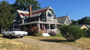 Une maison à deux étages avec un porche, une allée et une voiture blanche garée devant.