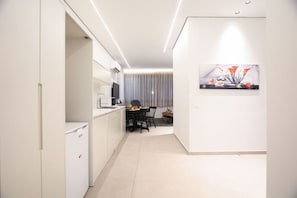 Une cuisine moderne avec des meubles blancs, un coin repas comprenant une table et des chaises, et un espace de vie doté d’une grande fenêtre et d’un tableau au mur.