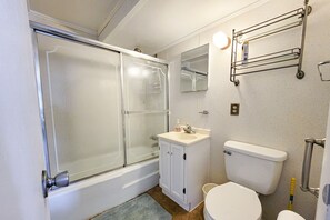 Kylpyhuone, jossa on lasiseinällä varustettu suihku, valkoinen pesuallas, wc ja pyyhekoukku.