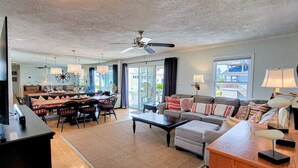 A spacious living room with a dining area, a ceiling fan, and large windows offering a view of the outside. - Fun, Chill, and Coastal Comfort at Hoot (Topsail Beach)