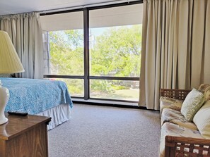 Quarto com uma janela grande, uma cama, um sofá e uma luminária.