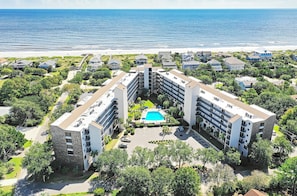 Un hôtel à plusieurs étages doté d’une cour intérieure où se trouve une piscine, le tout entouré d’une végétation luxuriante et offrant une vue sur la plage.