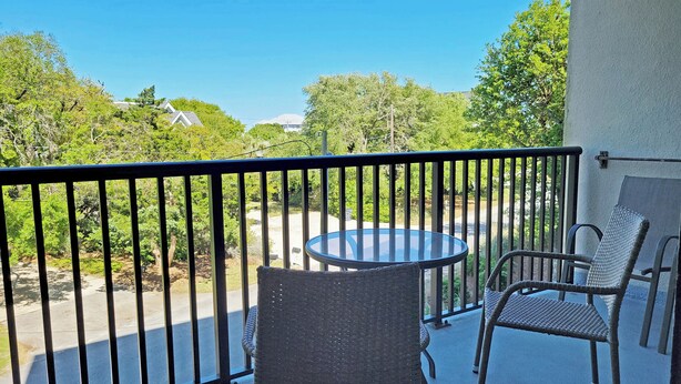 A balcony with a glass table and two wicker chairs, overlooking a road and greenery. - Townhouse Style Condo, Beach Access Across Road, Pool, Grilling Area, Elevator (Pawleys Island)