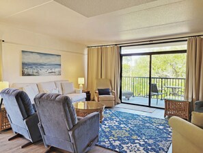 A hotel room with a sofa, armchairs, a coffee table, a painting, and a balcony with outdoor furniture.