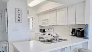 Uma cozinha moderna com armários brancos, forno embutido, micro-ondas, máquina de café e pia.