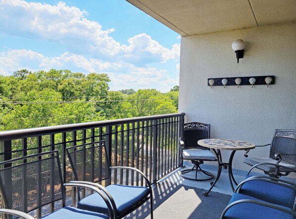 A balcony with outdoor seating, a wall-mounted light fixture, and a view of greenery.