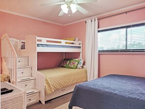 A bedroom with a bunk bed, a desk with drawers, a chair, a window with blinds, and a ceiling fan.