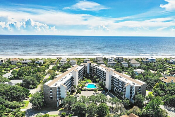A resort with a central pool, surrounded by lush greenery and beachfront properties. - Fifth Floor Condo across from Beach Access, Balcony, Pool, Grill Area, Elevator (Pawleys Island)