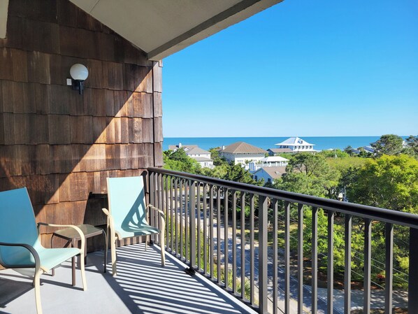 A balcony with a view of the sea, a wooden wall, and two chairs.