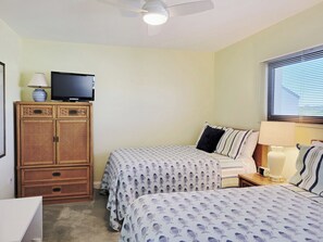 A bedroom with two beds, a television on a cabinet, and a window with blinds.