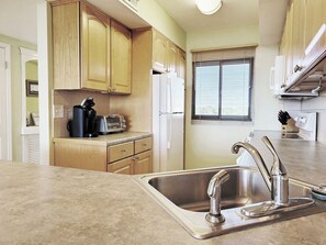 A kitchen with wooden cabinets, a stainless steel sink, and a window with blinds. - Top Floor Condo, Beach Access across Road, Balcony, Pool, Grill Area, Elevator (Pawleys Island)