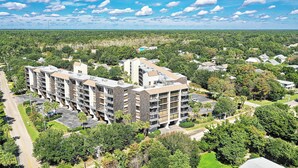 A multi-story residential building with balconies, surrounded by greenery and a clear sky. - Top Floor Condo, Beach Access across Road, Balcony, Pool, Grill Area, Elevator (Pawleys Island)