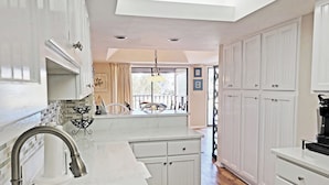 A modern kitchen with white cabinetry, a marble countertop, and a stainless steel sink.