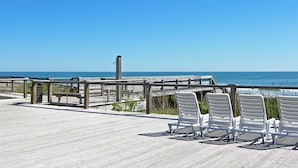 A wooden deck with white chairs overlooking the ocean.