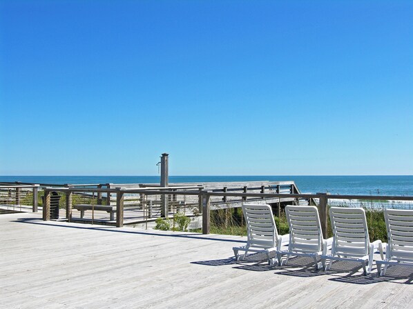 A wooden deck with white chairs overlooking the ocean.