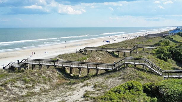 A beach with a wooden boardwalk leading to the shore, sandy beach, and ocean.