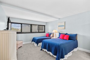 Quarto com duas camas, uma escrivaninha, luminária e janela com persianas.