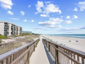 A wooden boardwalk leading to a beach with a hotel in the background.