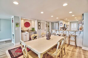 A spacious dining area with a large table and chairs, a kitchen with white cabinets, and a red decorative item on the wall. - Oceanside Townhouse-Style Condo, Ocean View, Private Patio, Beach Access, Pool (Pawleys Island)