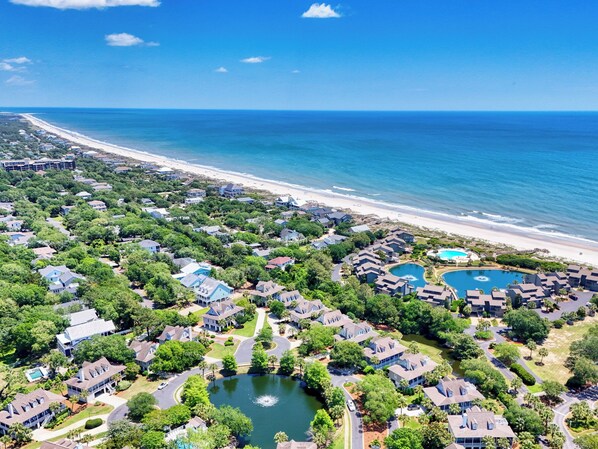 An aerial view of a coastal residential area with houses, a beach, and a lake.