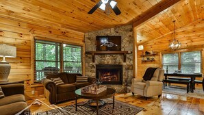 A cozy cabin interior with a stone fireplace, wooden walls, and a comfortable seating area.
