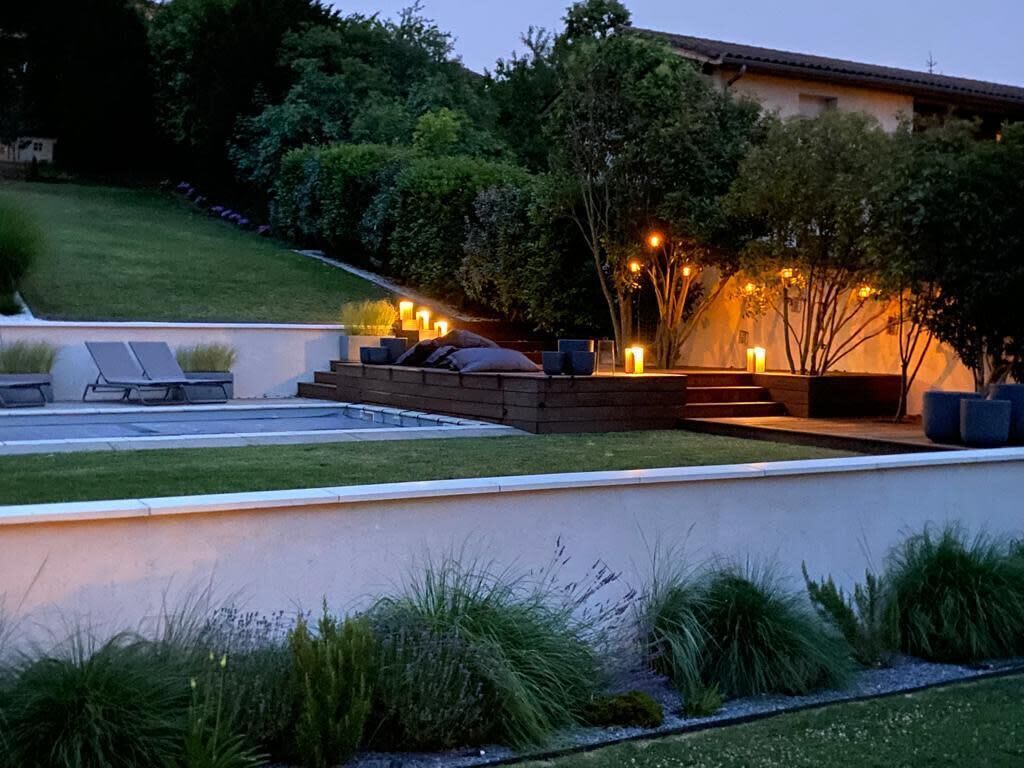 Ein angelegter Außenbereich mit Pool, Sitzgelegenheiten und Treppen zu einer überdachten Terrasse mit Kerzen.