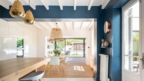 Une cuisine moderne avec une table en bois et des tabourets de bar, un coin repas avec des chaises et une grande fenêtre offrant une vue sur l’extérieur.