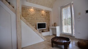 A modern interior with a stone wall, a flat-screen TV, a wooden bench, and a large window with curtains. - Lamia from the 5 chimneys (San Michele Salentino)