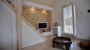 Un intérieur moderne avec un mur en pierre, un téléviseur à écran plat, un banc en bois et une grande fenêtre avec des rideaux.
