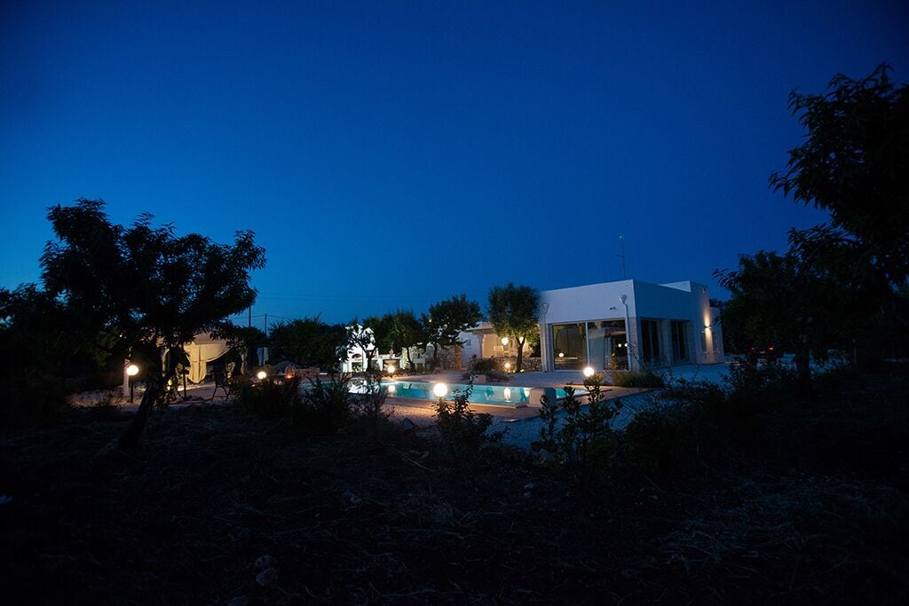 Une maison moderne avec une piscine, entourée d’arbres et illuminée par des éclairages extérieurs.