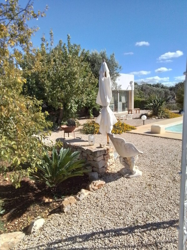 A garden area with a statue, a white umbrella, and a pool in the background.