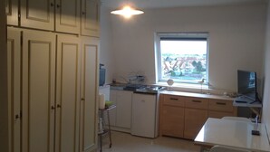 Een keuken met witte kasten, een raam, een spoelbak en een eethoek met tafel en stoelen.