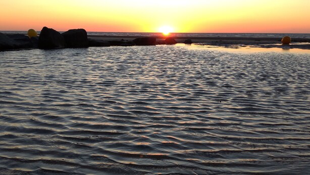 Een strand met kalm water en rotsen bij zonsondergang.