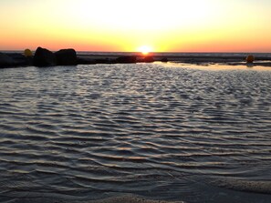 Une scène de plage avec une eau calme et des rochers au coucher du soleil.
