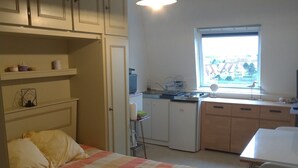 Een slaapkamer met een bed, nachtkastje, klein bureau en een raam.