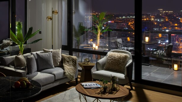 A modern living room with a sofa, armchair, and coffee table, featuring large windows with a city view at night. - G Tower Residences (Istanbul)