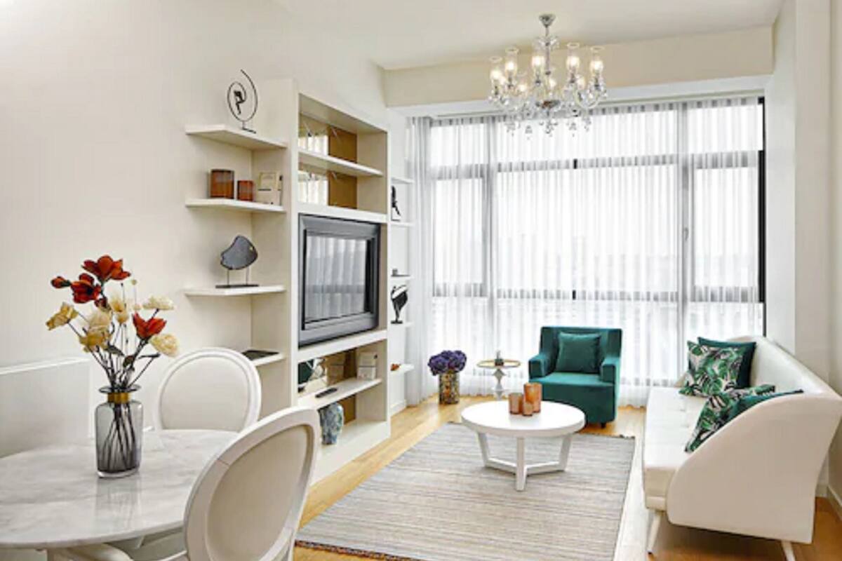 A modern living room with a white sofa, a dining table with chairs, a TV, and a chandelier.
