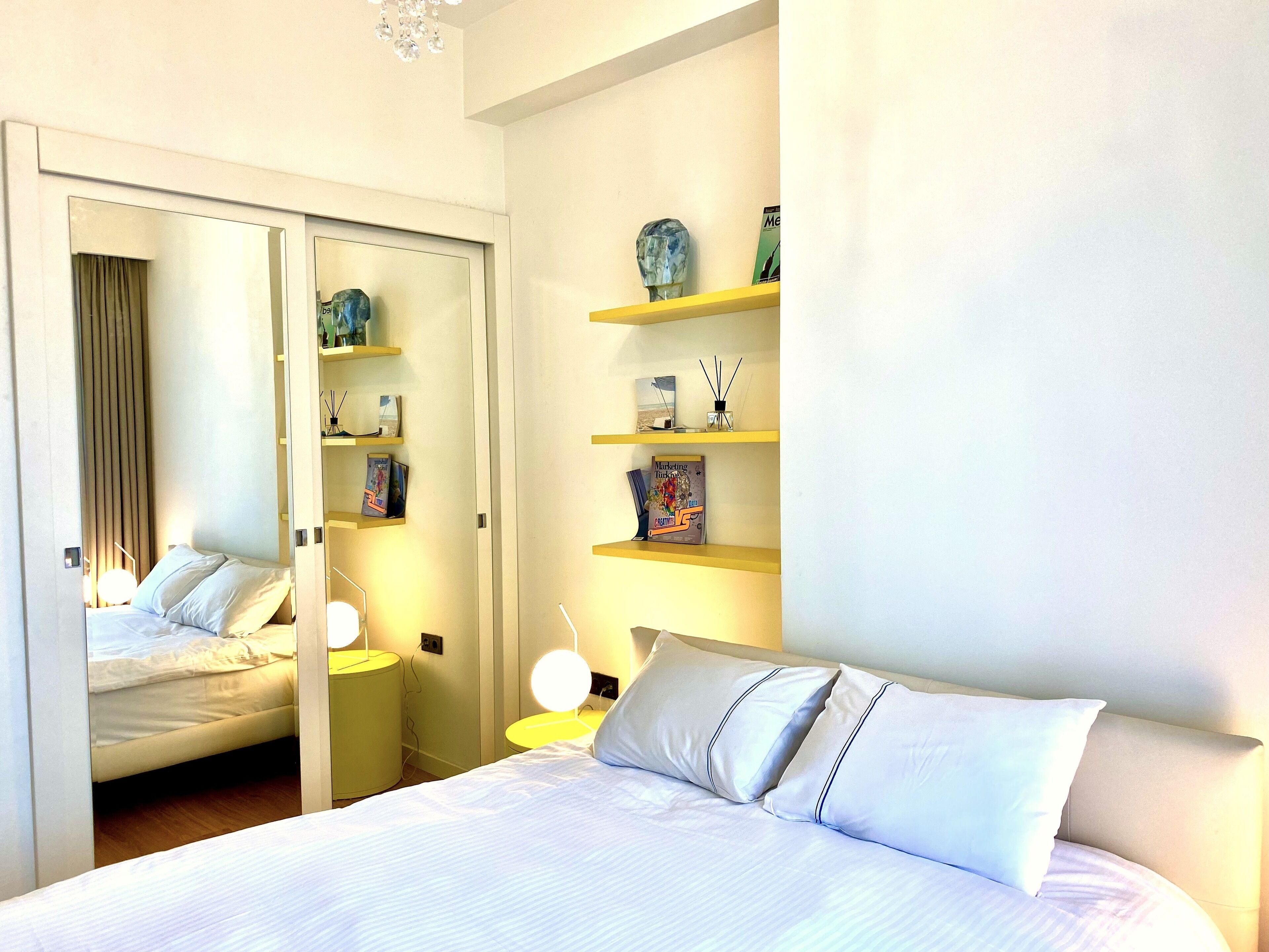 Una habitación de hotel con una cama, mesitas de noche, un espejo y estantes con adornos.
