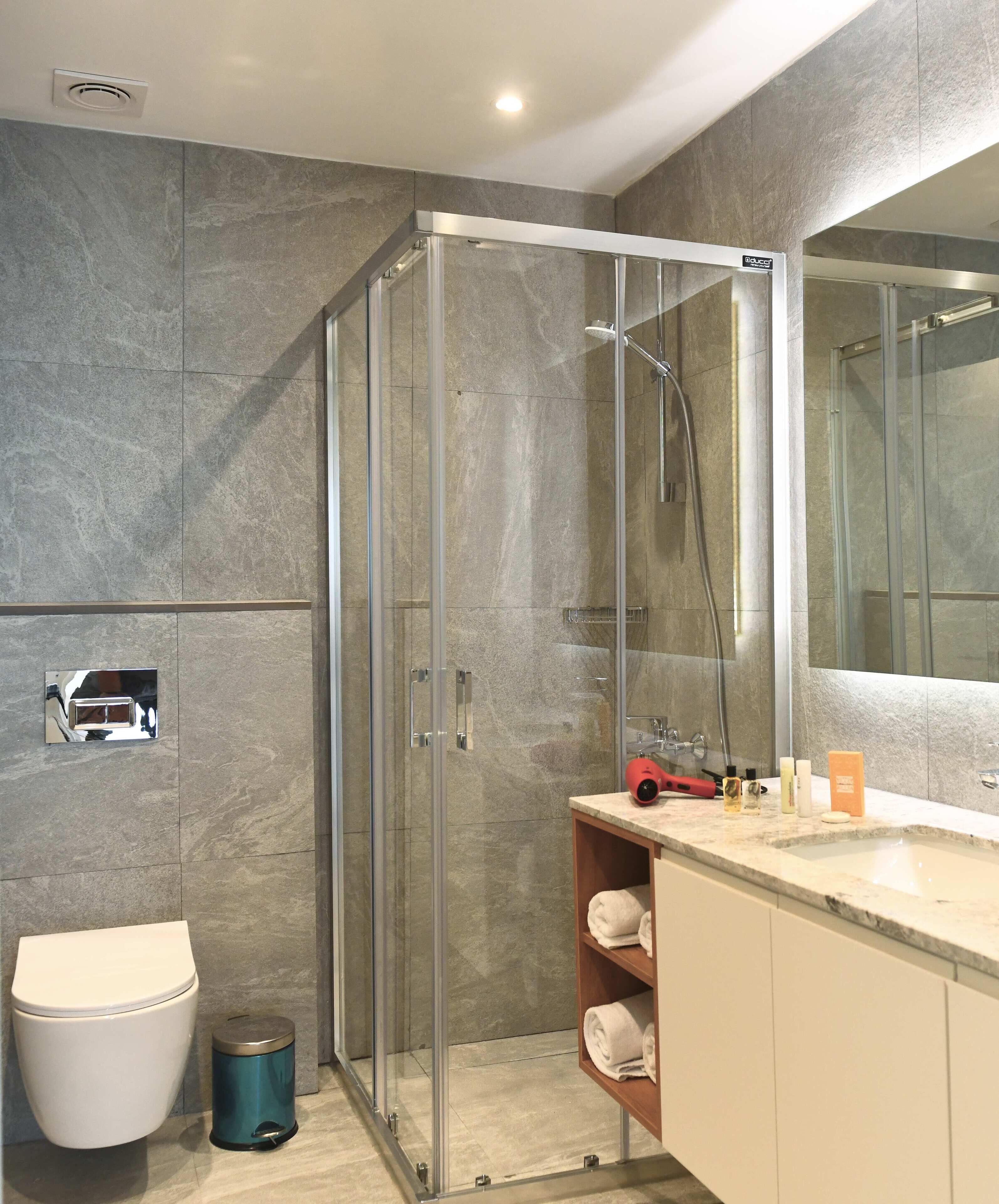 Un baño moderno con cabina de ducha de vidrio, inodoro, lavamanos con artículos de aseo y espejo.
