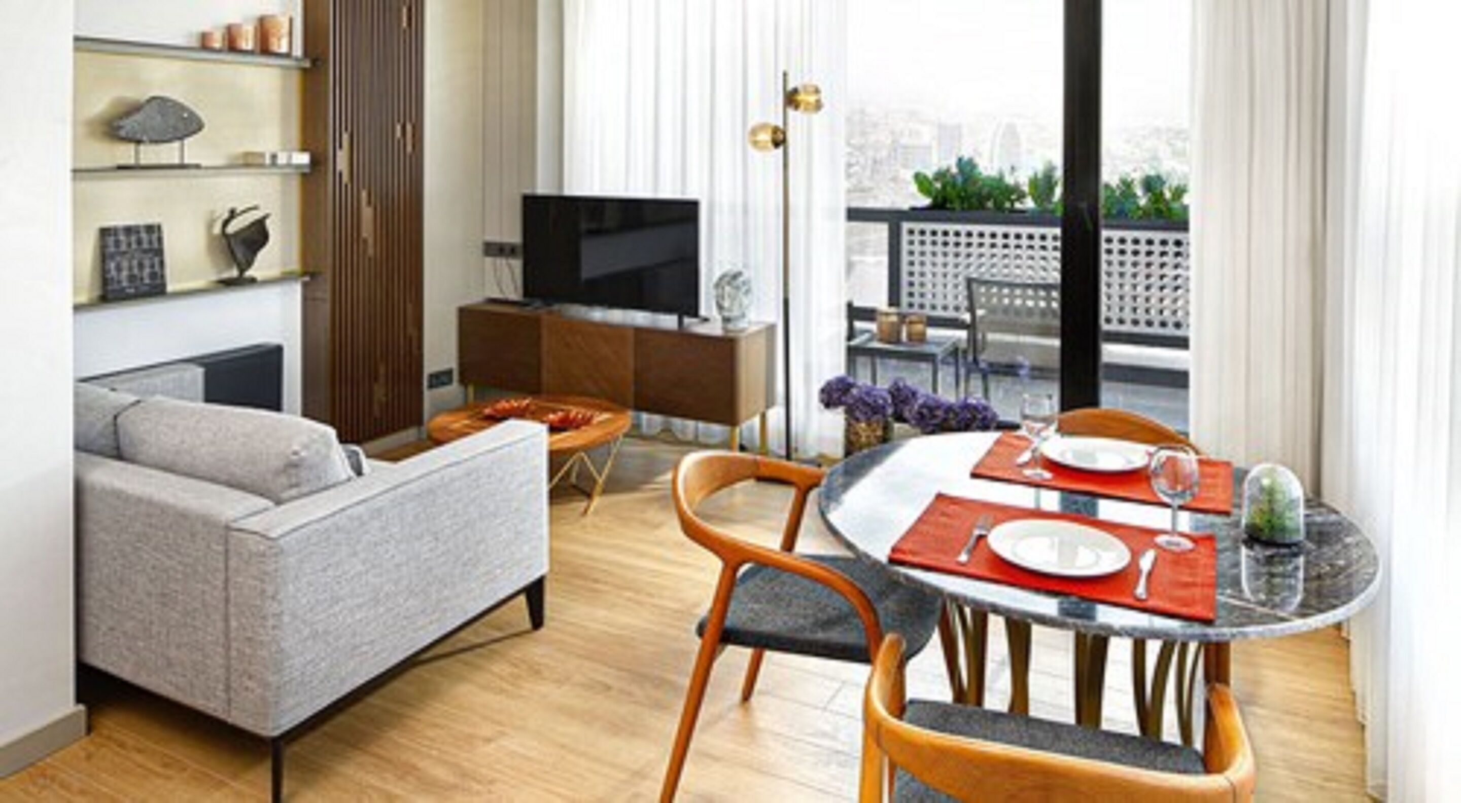 A modern living room with a sofa, a dining table set for two, a TV, and a balcony with a view.