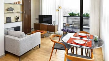 Una sala moderna con un sofá, una mesa de comedor para dos personas, un televisor y un balcón con vistas.