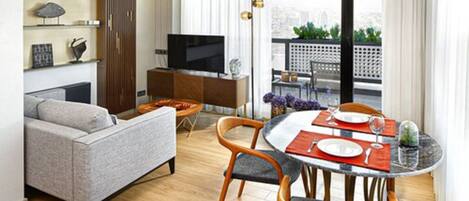 A modern living room with a sofa, a dining table set for two, a TV, and a balcony with a view.