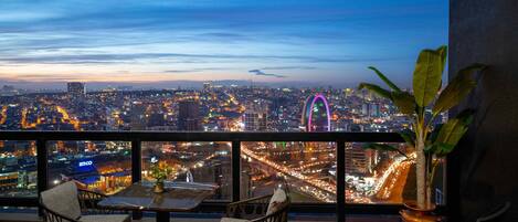A balcony with a city view at dusk, featuring a Ferris wheel and a busy street below.