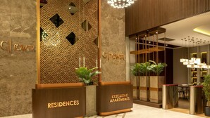 A hotel lobby with a modern design, featuring a reception desk labeled 'Residences' and 'Executive Apartments'. There is a decorative wall with geometric patterns and a hanging spherical light fixture. - G Tower Residences (Istanbul)