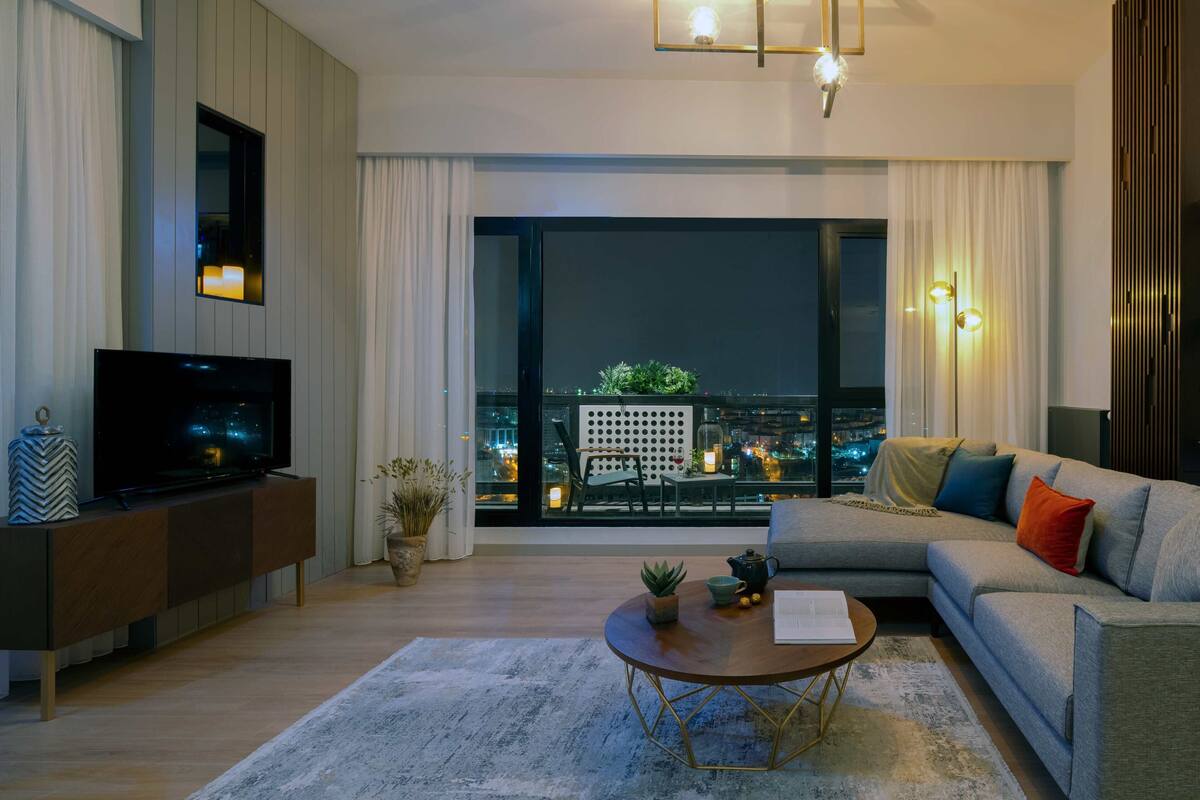 A modern living room with a large window, a flat-screen TV, a sofa, and a coffee table.