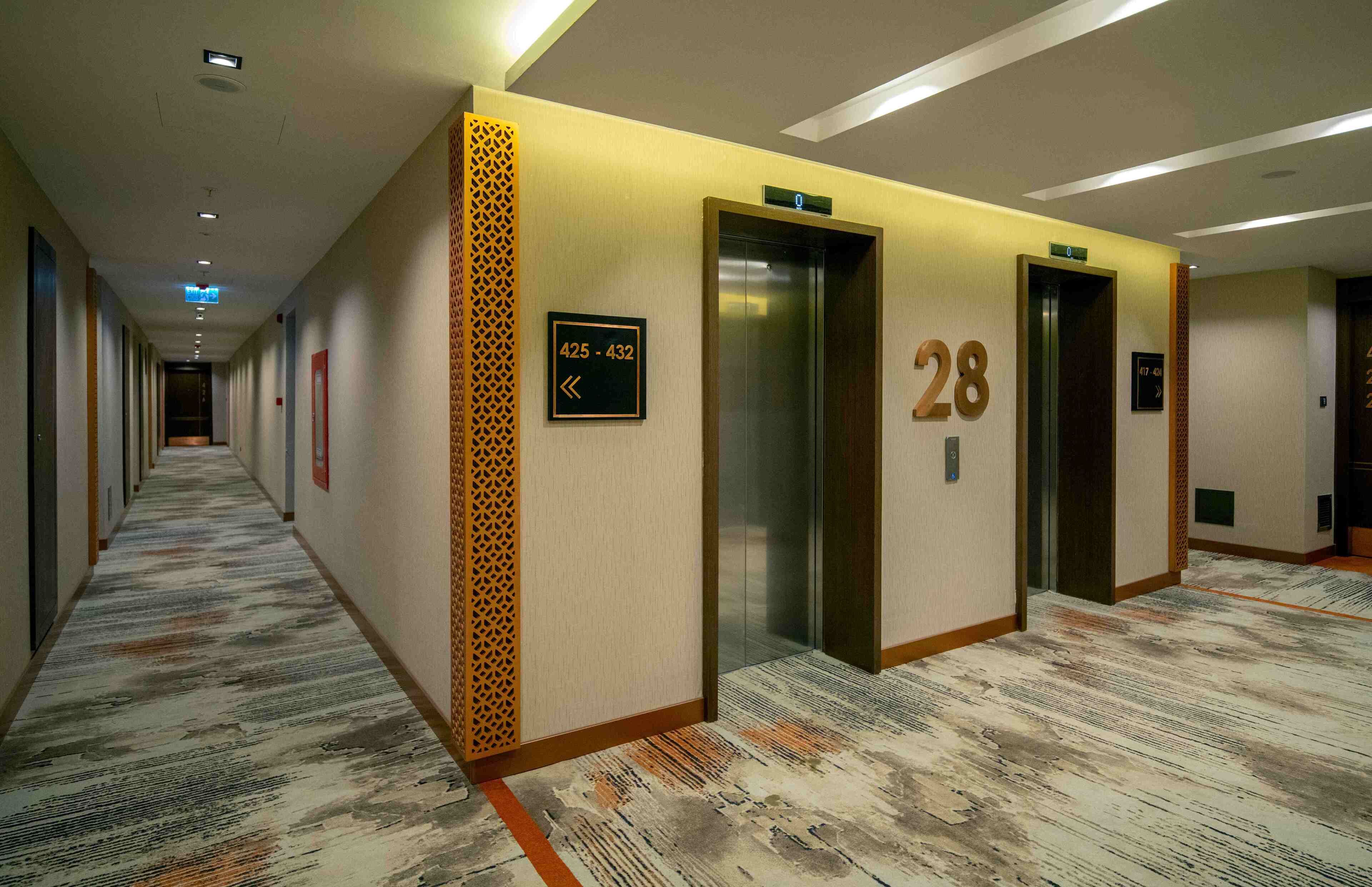A hotel corridor with a patterned carpet, numbered doors, and an elevator.